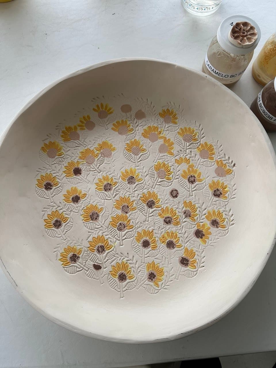 Una fuente grande de cerámica en proceso de pintura, con girasoles amarillos pintados a mano