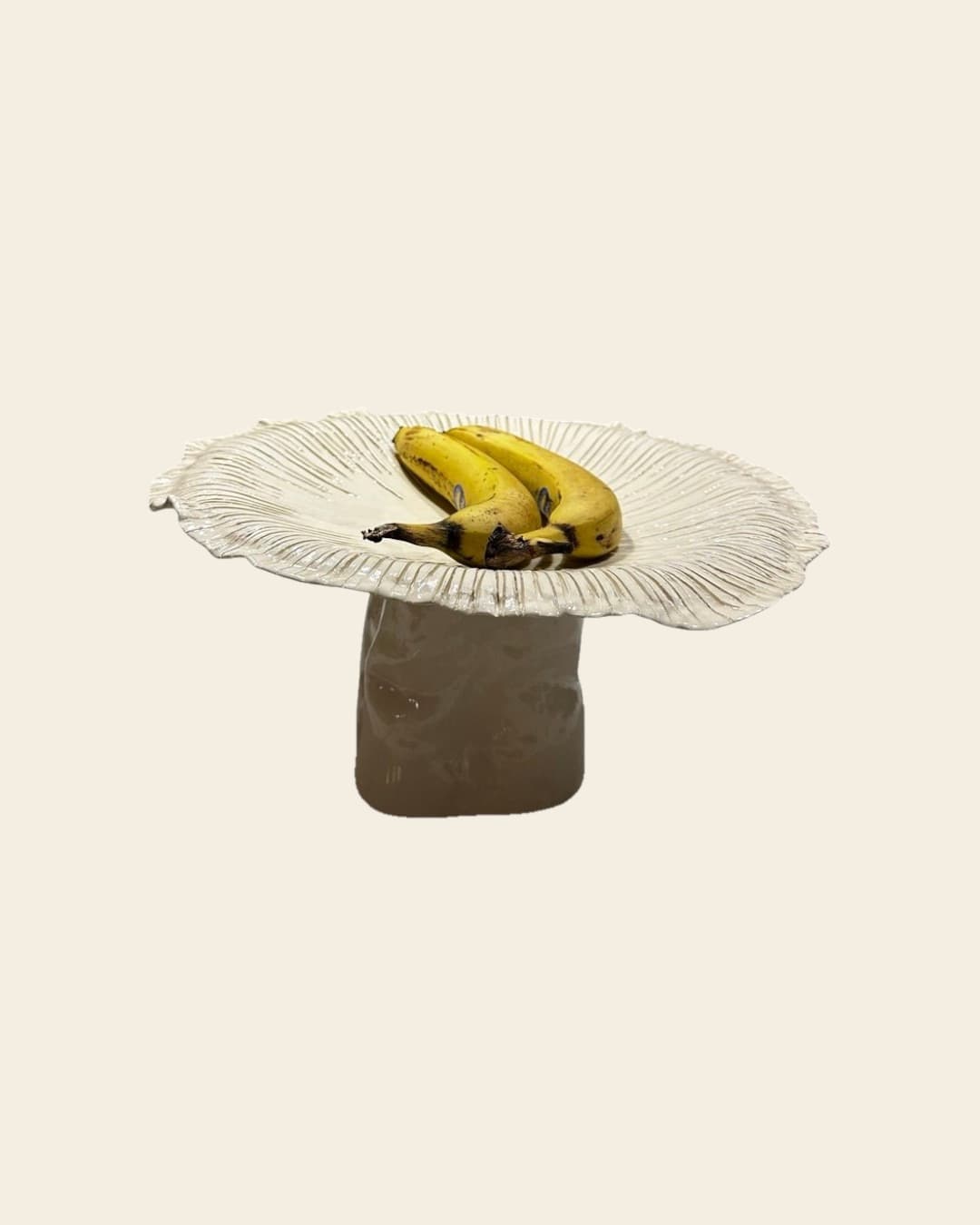 El Hongo Gigante usado como frutera, con bananas sobre el sombrero, sobre fondo beige