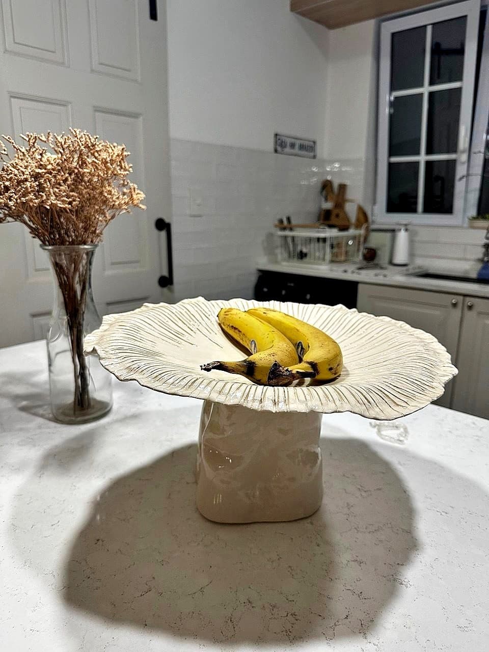Hongo gigante de cerámica hecho a mano, usado como frutera, con bananas sobre el sombrero
