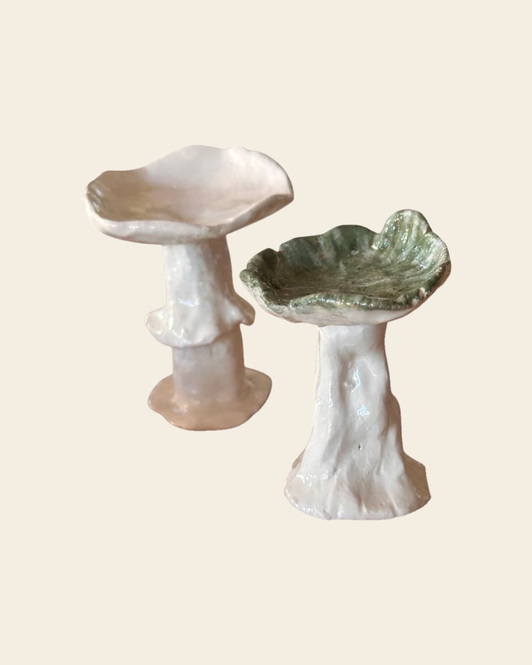 Dos hongos de cerámica modelados a mano sobre una mesa de madera, con ramitas de lavanda: uno todo blanco y otro con el sombrero verde y el tallo blanco